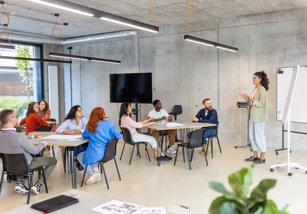 Businesswoman standing near a flipchart and guiding discussions with businesspeople seated in small groups.