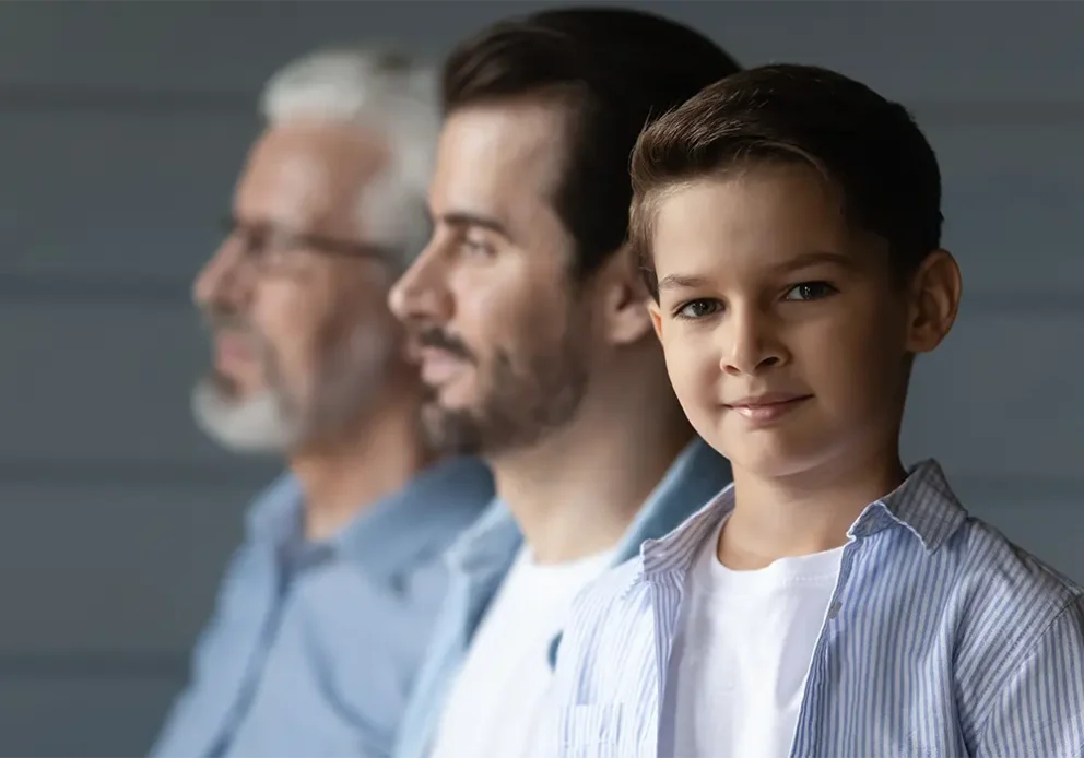 Portrait of happy small teen boy look at camera on grey wall background with young Caucasian father and older grandfather. Three generations of men show family unity and boding.