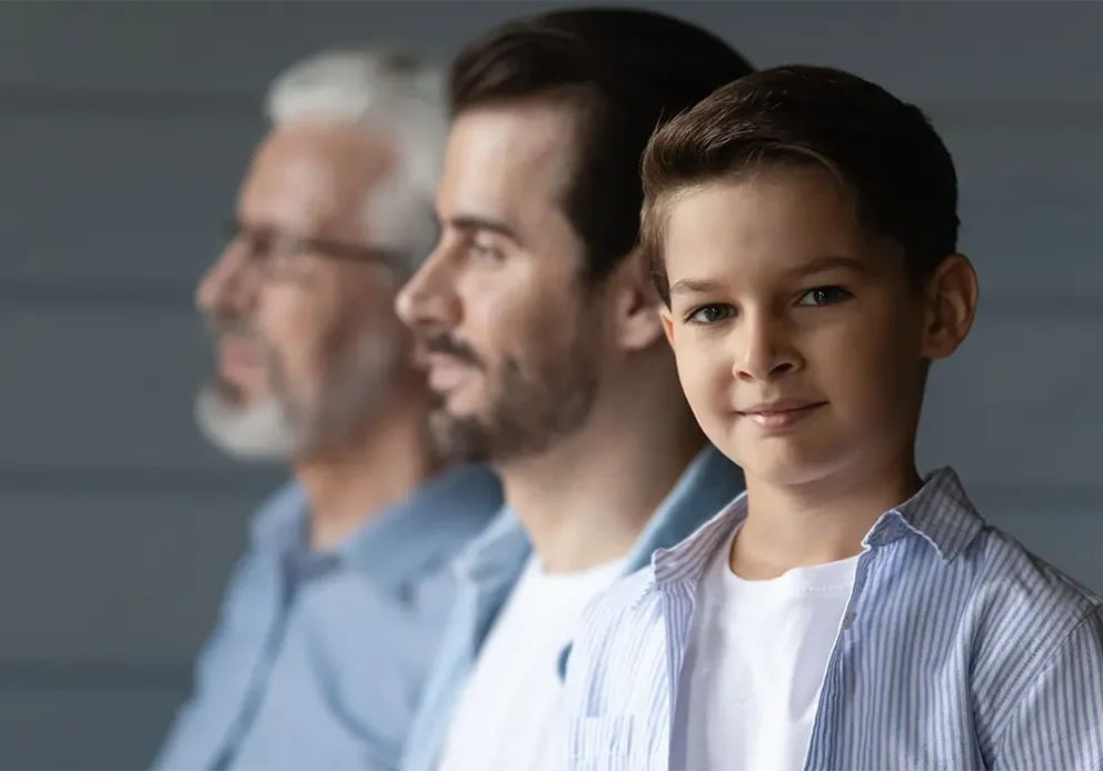 Portrait of happy small teen boy look at camera on grey wall background with young Caucasian father and older grandfather. Three generations of men show family unity and boding.
