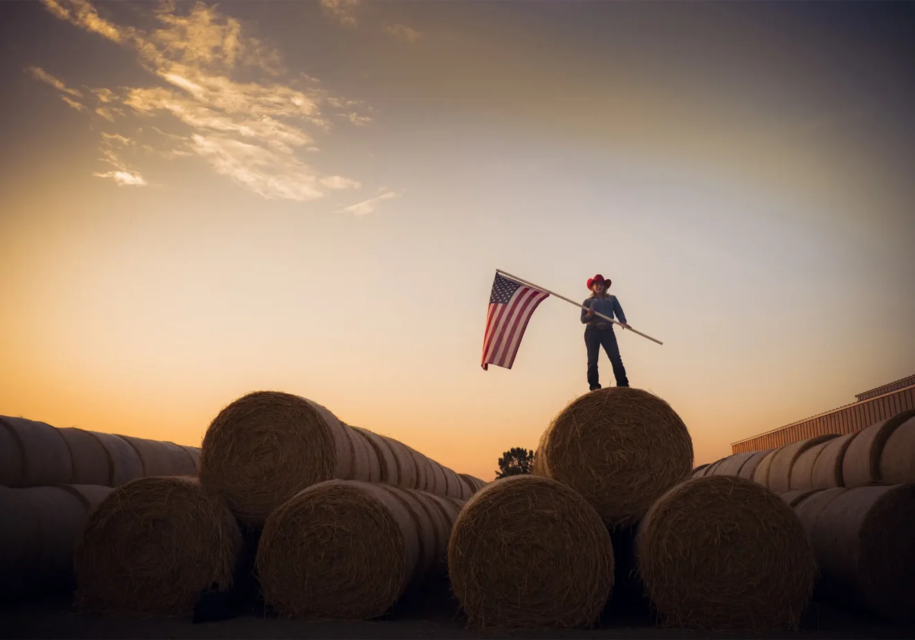Woman farmer holding American flag atop hay bales